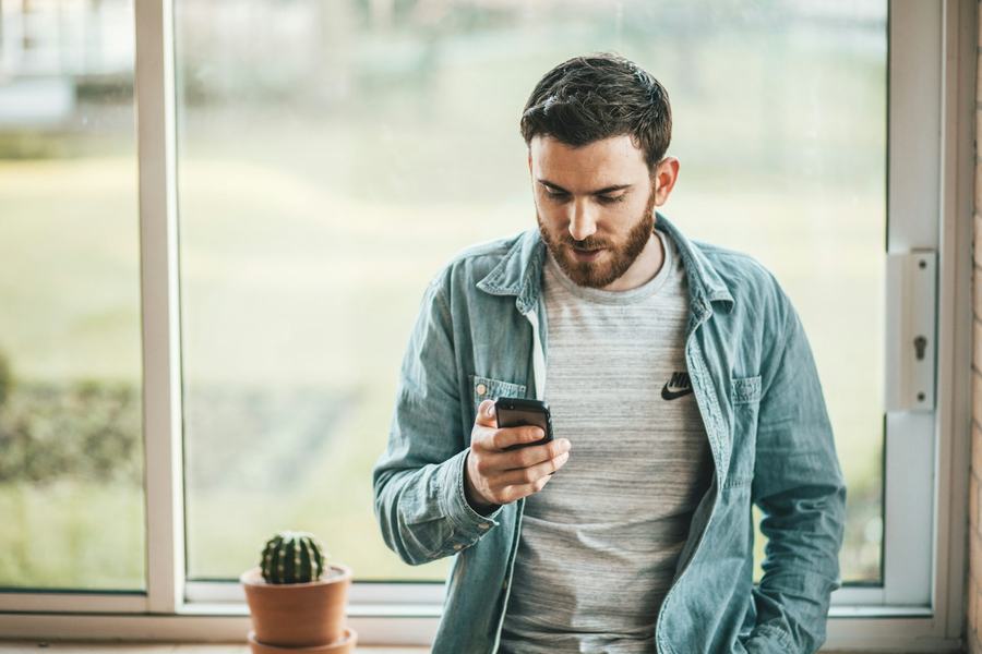 Mann sjekker mobilen ved et vindu